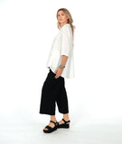 model in a white button down with a swirl texture. blouse has 3/4 sleeves and oversized rounded pockets at the hip. Worn with a wide leg black pant with the same texture