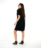 model in a black knee length dress with short sleeves and a round neckline. dress has a swirl texture and a diagonal seam across the body with a hidden seam pocket on the right
