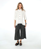 model in a white button down with a swirl texture. blouse has 3/4 sleeves and oversized rounded pockets at the hip. Worn with a wide leg black pant with white polkadots