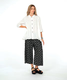 model in a white button down with a swirl texture. blouse has 3/4 sleeves and oversized rounded pockets at the hip. Worn with a wide leg black pant with white polkadots