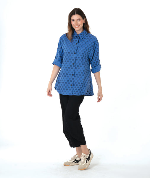 model in a black pant with a checkered blue and grey print button down blouse with rolled sleeves