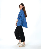model in a black pant with a checkered blue and grey print button down blouse with rolled sleeves