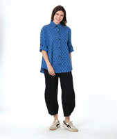model in a black pant with a checkered blue and grey print button down blouse with rolled sleeves