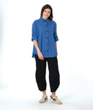 model in a black pant with a checkered blue and grey print button down blouse with rolled sleeves