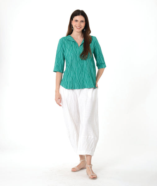 model in a barrel leg white pant with a matching teal pullover top with a 3/4 sleeve and an open flat collar