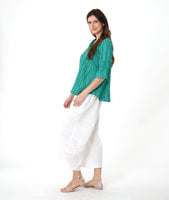 model in a barrel leg white pant with a matching teal pullover top with a 3/4 sleeve and an open flat collar