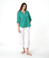model in a barrel leg white pant with a matching teal pullover top with a 3/4 sleeve and an open flat collar