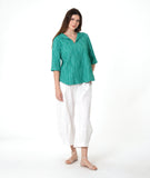 model in a barrel leg white pant with a matching teal pullover top with a 3/4 sleeve and an open flat collar