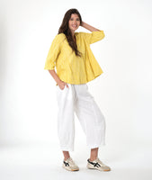 model in a white barrel leg pant with a matching yellow pullover top with 3/4 sleeves, a collar and a vneck