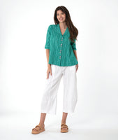 model in a white barrel leg pant, with a matching teal button down blouse with a flat open collar and a 3/4 sleeve with a large cuff