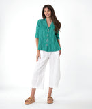 model in a white barrel leg pant, with a matching teal button down blouse with a flat open collar and a 3/4 sleeve with a large cuff