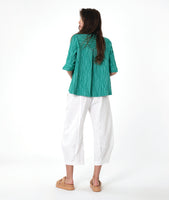model in a white barrel leg pant, with a matching teal button down blouse with a flat open collar and a 3/4 sleeve with a large cuff