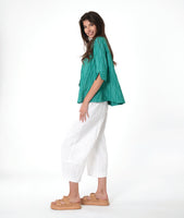 model in a white barrel leg pant, with a matching teal button down blouse with a flat open collar and a 3/4 sleeve with a large cuff