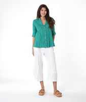 model in a white barrel leg pant, with a matching teal button down blouse with a flat open collar and a 3/4 sleeve with a large cutff