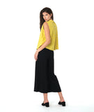 model in a black pant with a checkered yellow and grey print button down sleeveless blouse with a boxy body and a twin button detail