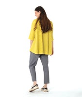 model in a grey pant with a checkered yellow and grey print button down blouse with a full body and dipped hem in the back.