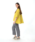 model in a grey pant with a checkered yellow and grey print button down blouse with a full body and dipped hem in the back.