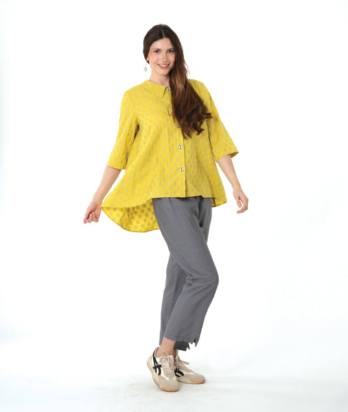 model in a grey pant with a checkered yellow and grey print button down blouse with a full body and dipped hem in the back.