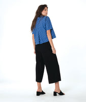 model in a black pant with a checkered blue and grey print button down blouse with short sleeves and a cropped body