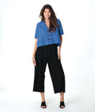 model in a black pant with a checkered blue and grey print button down blouse with short sleeves and a cropped body