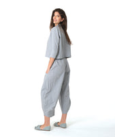 model in a blue and grey pinstripe short, boxy button down with a 3/4 sleeve and flat open collar. worn with a matching barrel leg pant