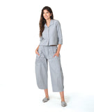 model in a blue and grey pinstripe short, boxy button down with a 3/4 sleeve and flat open collar. worn with a matching barrel leg pant