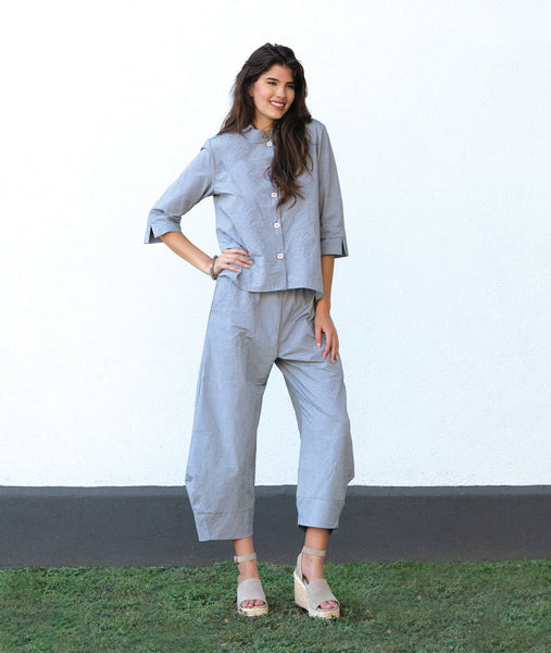 model in a blue and grey pinstripe  button down with a 3/4 sleeve and double collar. worn with a matching barrel leg pant