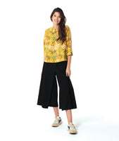 model in a wide leg black pant with overlapping panels, worn with a yellow button down blouse with a multi color leaf print