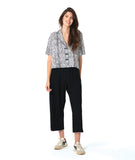 model in a straight leg black pant, worn with a black and white striped blouse with twin buttons, short sleeves, and an open, flat collar
