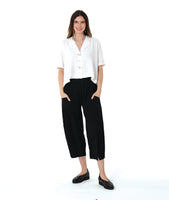 model in a wide leg black pant with a boxy white button down blouse with an open, flat collar and a twin button detail
