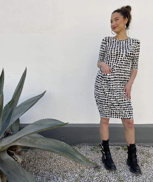model in a black and white dot print tunic with a curved hip pocket set into a diagonal seam across the body
