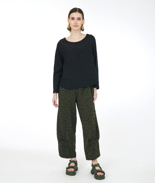 model in a wide leg distressed olive pant with a pucker at each calf, and a matching boxy black top with long sleeves