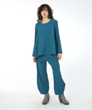 model in a wide leg blue pant with a matching flowy top with long sleeves and a single squared pocket at the hip.