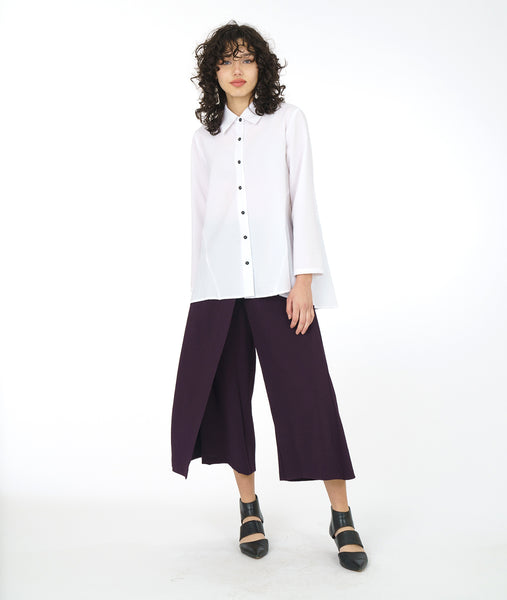 model in a white button down blouse with a lower hem in the back, worn with an eggplant color wide leg pant with an overlapping panel on the front