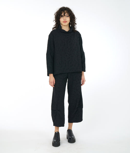 model in a distressed black pant with a matching boxy top with princess seams, long sleeves and a cowl neck