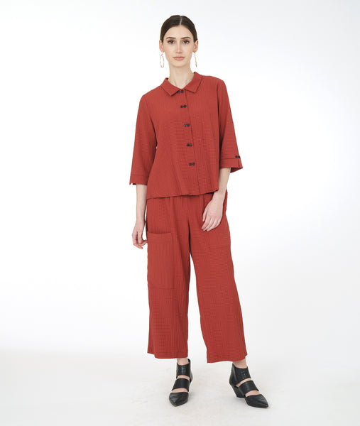 model in a rust color button down blouse with a 3/4 sleeve and a twin button detail, worn with a wide leg pant with an asymmetrical cargo pocket