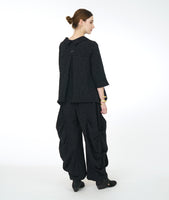 model in a wide leg distressed black pant with dramatic pleating on the sides, worn with a matching button down top with 3/4 sleeves and a rounded collar