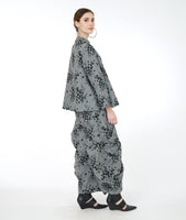 model in a wide leg grey print pant with a large pleat detail along the sides, worn with a matching jacket with a boxy body and a slight standing collar