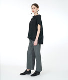 model in a boxy black top with a cowl neck, and a wide leg grey pant with a small split at either ankle