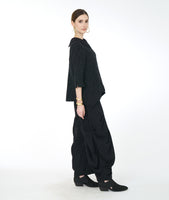 model in a wide leg distressed black pant with dramatic pleating on the sides, worn with a matching button down top with 3/4 sleeves and a rounded collar