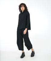 model in a distressed black wide leg pant with a pleat at either calf, with a matching boxy top with a cowl neck