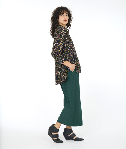 model in a black terrazzo print button down blouse with a mandarin style collar and a low drape in the back, worn with a wide leg green pant