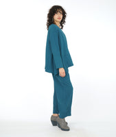 model in a wide leg blue pant with a matching flowy top with long sleeves and a single squared pocket at the hip