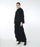 model in a wide leg distressed black pant with a large dramatic pleating detail on the sides, worn with a matching black boxy cowl neck top