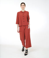 model in a rust color button down blouse with a 3/4 sleeve and a twin button detail, worn with a wide leg pant with an asymmetrical cargo pocket