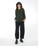 model in a distressed black pant with a matching olive green top with long sleeves and a small  triangular placket with a single button at the neckline