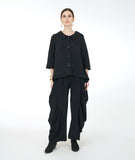 model in a wide leg distressed black pant with a large dramatic pleating detail on the sides, worn with a matching black button down blouse