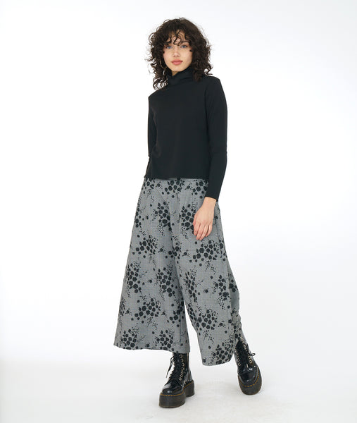 model in a wide leg grey patterned pant, with a black mock turtleneck top