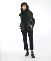 model in a slim black pant with a black turtleneck and a green distressed jacket with a drawstring collar, triangle buttons and pockets