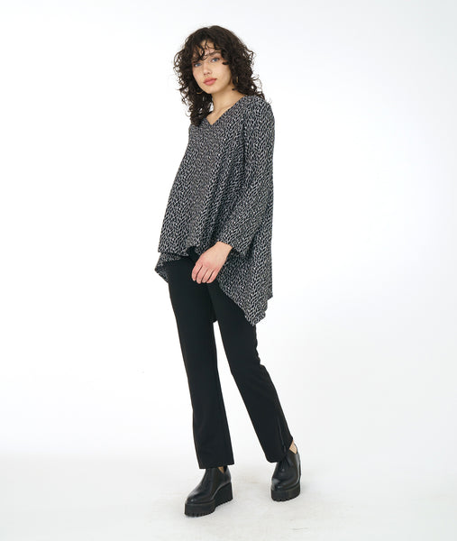 model in a black straight leg pant, worn with a black and white leaf print tunic with long sleeves, a v-neck and a low double point drape in the back 